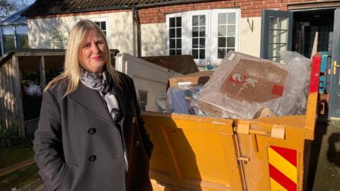 Anna Mimms is pictured outside her home at Woodborough in Nottinghamshire. She is shown standing by a skip which is filled with flood-damaged items from her home