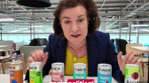 Eluned Morgan looking into the camera, smiling, with six cocktail cans in front of her