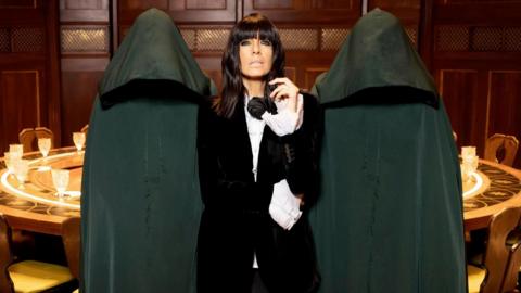 Claudia Winkleman surrounded by anonymous green-cloaked Traitors 
