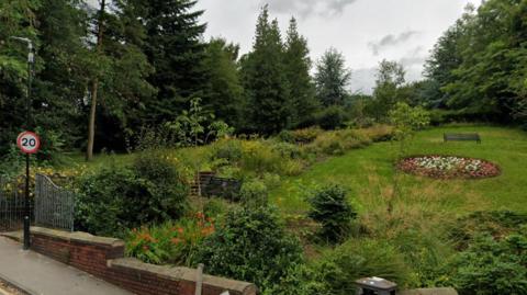General view of Scarth Gardens in Morley, Leeds, showing a green park with a round central flower bed and trees
