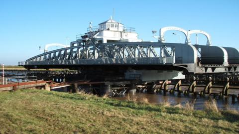 The steel structure of the bridge has been swung at a right angle to the road to allow boats to continue up the River Nene.