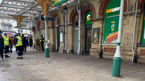 The outside of a railway station. There is a large yellow and green Subway signages displayed on the windows. 
