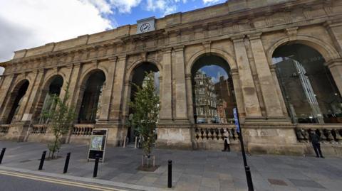 Front of Central Station. It is a tall building made of yellow stone with six large archways across the facade.