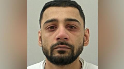 Akaash Ibra's mugshot. He has short dark hair and a beard