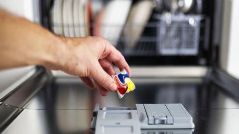 Persons arm putting a dishwasher tablet into a dishwasher.