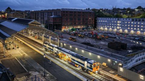 An overhead shot of upgrade works taking place at Huddersfield station. It is taken during the evening with lights illuminating the track.