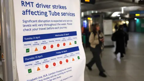 People walk past a sign in a Tube station warning about strike action