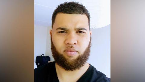 A man with a beard and short brown hair is looking at the camera in this selfie. He is wearing a dark-coloured top.