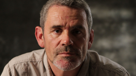 Paul Conroy poses for a headshot. He has short greying hair and stubble.