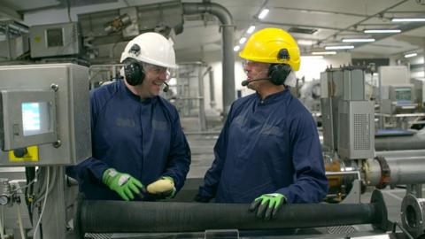 Two people in a factory. One is holding a potato