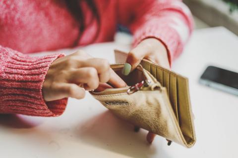 A close-up of a woman's hands. She is wearing a pink jumper and is reaching into a gold purse to take out money. 