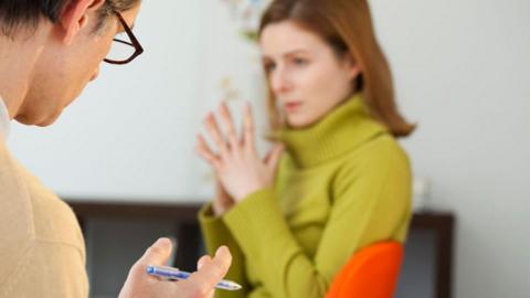 A therapist holding a pen and speaking to a patient.