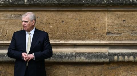 Prince Andrew stands with his back against a stone wall