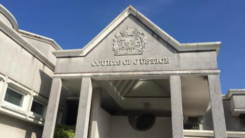 Outside of Truro Crown Court, a grey stone building with the courts of justice logo on the front. 
