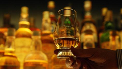 A hand holding a glass with a small amount of whisky in it