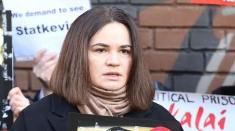 Exiled Belarusian opposition leader Svetlana Tikhanovskaya (C) holds a photo of her jailed husband Sergei Tikhanovsky as she speaks with journalists during a protest in front of the Belarusian Embassy in Vilnius, Lithuania, on March 8, 2024