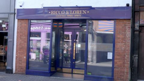 A purple shop front with "Ricco & Loren - cocktails, wines, sprits" written in gold lettering on a fascia board above the doors.