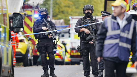 Armed police at the scene, with police vehicles in the background.