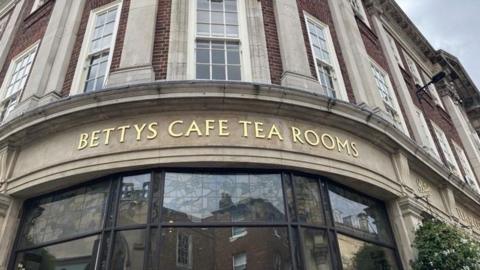 A gold sign for Bettys Cafe and Tea Rooms above glass windows