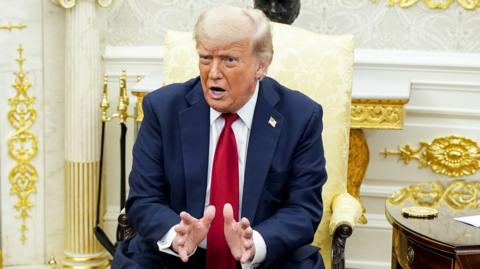 Donald Trump in the Oval Office wearing a blue suit and red tie