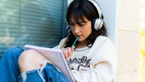 Pensive girl doing homework sitting next to a window outdoors - stock photo