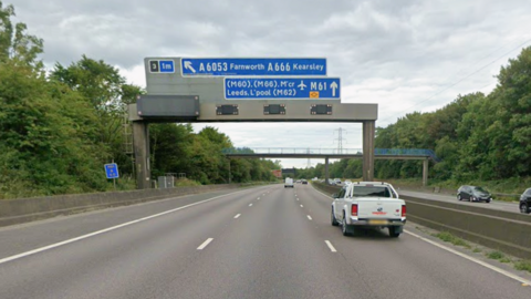 Cars on M61motorway with blue signs overhead at junction 3 slip road to Bolton