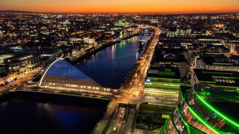 An aerial view of Dublin at night. Lights are on across the city and on a bridge across the River Liffey. 