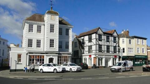 Bicester Market Square. There is a large white clock building next to a black and white Tudor-style building.
