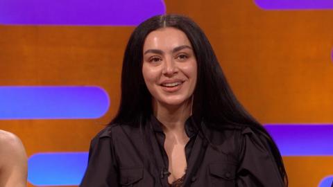 Charli XCX smiles. She has long black hair and wears a black shirt 