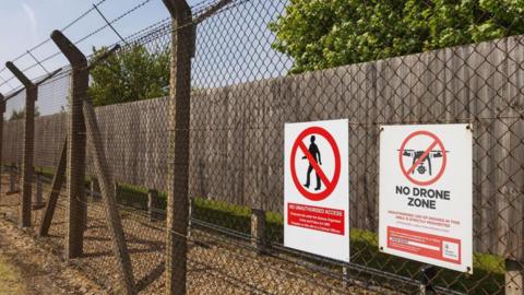 A chain-link fence with barbed wire at RAF Lakenheath displaying a warning sign that says drones are prohibited