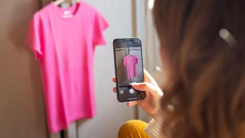 Woman taking a photo of a pink top hanging from a wardrobe door