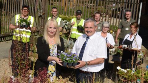 Sunderland City Council deputy leader Kelly Chequer and managing director of Bishopwearmouth Co-operative Shaun Donnelly hold flowers ready to be planted. Seven volunteers stand in the background.
