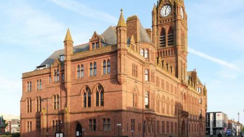 A huge ornate brick building with a clock tower on a street corner, which is Barrow Town Hall.