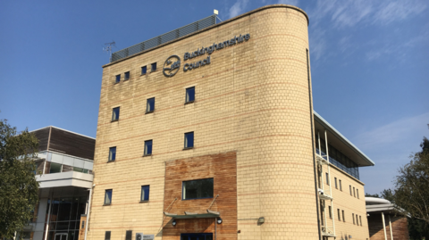 A picture of the Gateway building, which is the headquarters of Buckinghamshire council in Aylesbury. It is a five storey cream coloured building, and there is blue sky in the background.