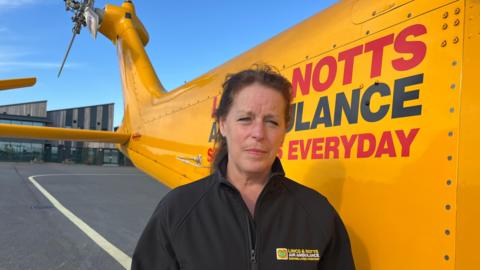 A woman wearing a branded fleece stands in front of the LNAA ambulance.