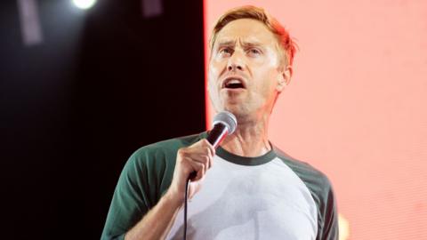 Russell Howard speaks into a microphone at Reading Festival