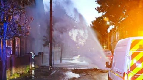 A burst water pipe in Leicester spraying water into the road. A highways maintenance van is in front of the burst water pipe