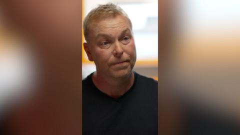 A blonde man, Sir Chris Hoy, in a black t shirt.