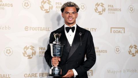 Nico O'Reilly wearing a suit holds the PFA Young Player of the Year trophy