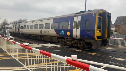 A two carriage Northern train is at a level crossing