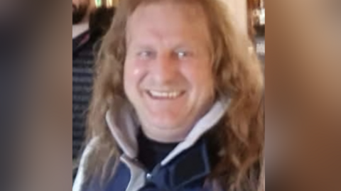 Imrich, who has long blond hair and is wearing a blue and white coat, smiles at the camera