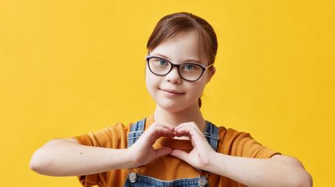 A young girl makes a heart symbol with her hands.