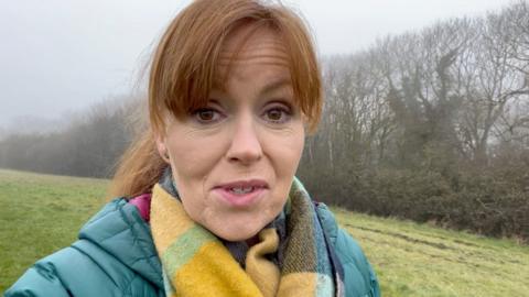 jenny rees standing in a field. She is wearing a green winter coat and a yellow scarf