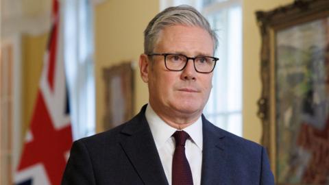 A handout photo made available on 21 September 2025 by Number 10 Downing Street of British Prime Minister Keir Starmer recording a video message in London, Britain, 19 September 2025. Starmer gave a statement on the recognition of Palestine by the UK Government. Starmer wears a navy suit with a white shirt and dark red tie. He wears square black rimmed glasses and looks straight away from the camera. 