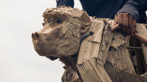 A close up of the face and part of body of a life-sized ape made from cardboard and plywood.