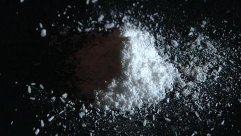 On a black table, a small pile of white powder lies. 