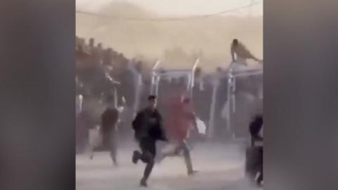 A crowd of people, one climbing over a fence, run to collect aid