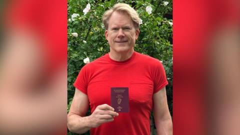 Prof Portmann is smiling and holding his Irish passport 