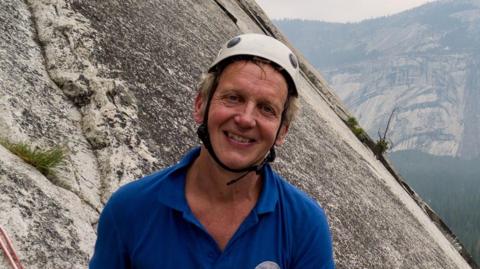 Stephen Lismore wearing a blue polo shirt and a climbing helmet smiling. 