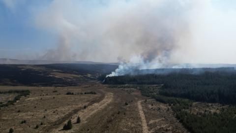 A vast landscape of fields and mountains, with smoke billowing in the distance